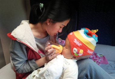 Qin Danliu, the mother of 5-year-old Chinese boy Hao Hao, who is diagnosed with severe brain tumor and Hydrocephalus, feeds her son on a train from Beijing to Shanghai, 9 April 2018 clipart