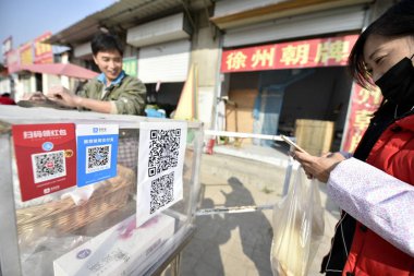 A customer has a QR code via mobile payment service Alipay of Alibaba Group on her smartphone scanned to pay her purchases at a roadside stall in Linyi city, east China's Shandong province, 26 December 2017 clipart