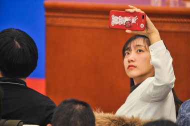 A reporter takes a photo with her smartphone during the news conference for the first session of the 13th National Committee of the Chinese People's Political Consultative Conference (CPPCC) in Beijing, China, 4 March 2018. clipart