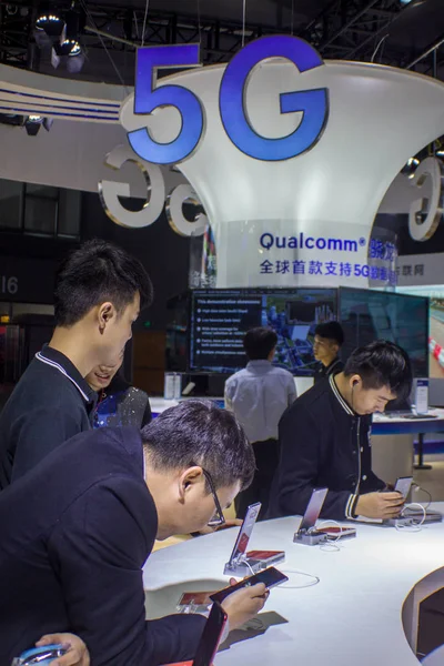 訪問者は 中国南部の広東省広州市で開催された中国モバイルグローバルパートナーカンファレンス2017の間 クアルコムのスタンドで5Gのロゴの前でスマートフォンを試してみる 2017年11月25日 — ストック写真