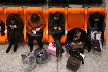 Passengers use their smartphones in massage armchairs while they are waiting for trains at the terminal of the Dalian North Railway Station in Dalian city, northeast China's Liaoning province, 3 December 2017 clipart