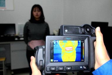 A Chinese worker uses a forward-looking infrared (FLIR) camera to test the heating ability of a product made of China's first far infrared conductive heating fiber developed based on carbon nano materials at a fiber company in Binzhou city, east Chin clipart
