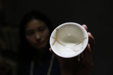 Chinese Kintsukuroi master Huang Junling shows the pottery cup repaired by her at a studio in Xi'an city, capital of northwest China's Shaanxi province, 2 March 2017 clipart