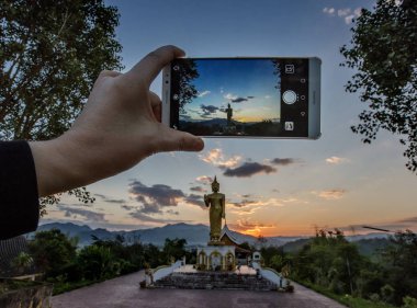 A local woman uses a Huawei smartphone to take photos at Wat Xieng Thong Temple in Muang Xay, Oudomxay Province, Laos, 30 January 2017 clipart