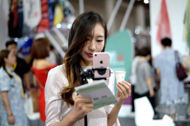 A Chinese webcasting hostess uses her smartphone to make live streaming webcast during an expo in Ji'nan city, east China's Shandong province, 1 September 2017 clipart
