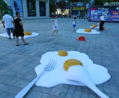 Local residents pose for photos with giant artworks featuring the shape of fried eggs in front of a shopping mall in Shaoxing city, east China's Zhejiang province, 7 August 2017 clipart