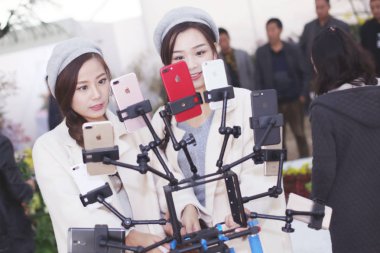 Chinese twin sisters Fei Fei and Fang and Fang who are online celebrities make live streaming webcast with several smartphones as they attend a chrysanthemum exhibition in Kaifeng city, central China's Henan province, 15 October 2017 clipart