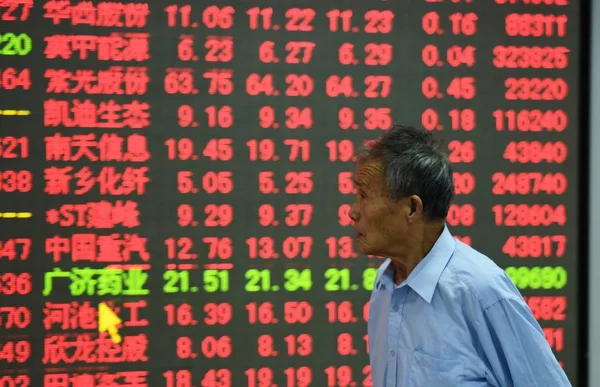 在中国东部浙江省杭州市一家股票经纪公司 一位中国投资者走过显示股价的屏幕 价格上涨为红色 价格下跌为绿色 — 图库照片