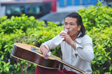 Chinese singer Yu Heqing drinks water during a break of his daily performance on the street in Nanning city, south China's Guangxi Zhuang Autonomous Region, 6 November 2016 clipart