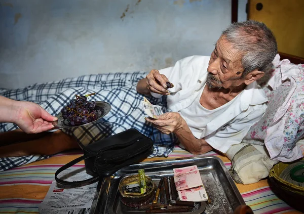 103歳のリン Yongqing は銀行のレジ係だったがぶどうを食べて 中国四川省南西部の成都にある自宅のベッドで紙幣を数え 8月1日に2016 — ストック写真