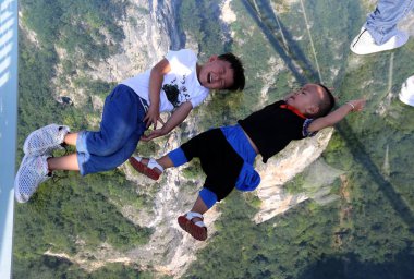 Young boys lie on the world's longest and highest glass-bottomed bridge over the Zhangjiajie Grand Canyon at Wulingyuan Scenic and Historic Interest Area in Zhangjiajie city, central China's Hunan province, 20 August 2016 clipart