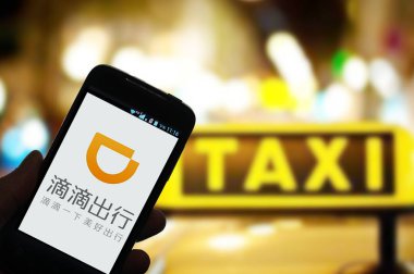 A Chinese mobile phone user uses taxi-hailing and car-service app Didi Chuxing on his smartphone in Jinan city, east China's Shandong province, 2 July 2015 clipart