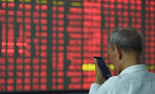 2016 日中国東部の浙江省杭州市の証券会社の家で 赤の価格上昇 と価格下落のため緑の株式の価格を表示する画面の前に彼のスマート フォンは 中国投資家 — ストック写真
