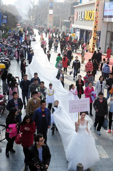 2016年3月13日 中国東部山東省済南市で行われたプロモーションイベントで ウェディングドレス会社の若い子供やスタッフが運んだ長さ101メートルのテールを持つブライダルガウンを着たモデルが通りをパレードします — ストック写真
