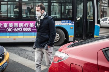 A foreigner wearing a face mask walks across a road in heavy smog in Beijing, China, 9 December 2015 clipart