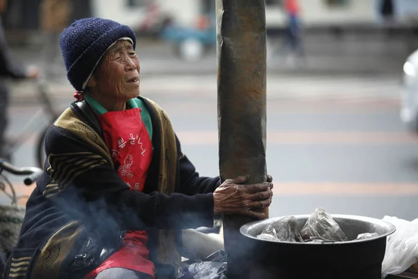 80歳の女性は 2015年9月14日 中国北東部の黒龍江省平河市の道路でゆで卵を売りながら ストーブで自分を温める — ストック写真