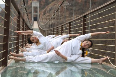 Chinese enthusiasts perform yoga on the 180-meter-high and 210 meter-long glass-bottomed suspension bridge in Fuxi Mountain in Xinmi city, central China's Henan province, 23 March 2016 clipart
