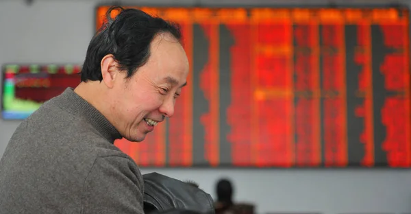 在中国东部江苏省南京市一家股票经纪公司 一位中国投资者在显示股价 价格上涨为红色 的屏幕前微笑 — 图库照片