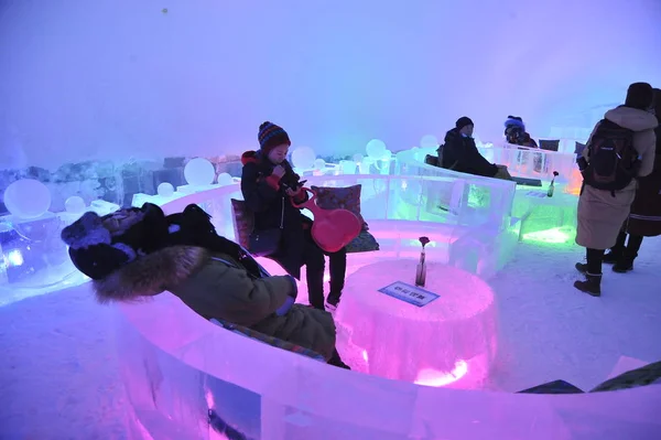 観光客は 中国ハルビン氷と雪世界 2019 ハルビン市 中国北東部の黒龍江省 2019 日の間に革新的な氷シェル テクノロジで構築されたアーチ形の氷のバーで氷椅子に座る — ストック写真
