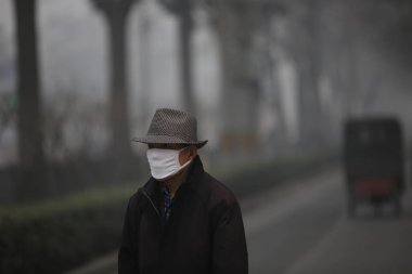A pedestrian wearing a face mask walks on a road in heavy smog in Beijing, China, 22 December 2015 clipart