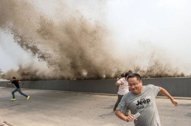 Visitors and local residents run away as waves from a tidal bore surge past a barrier on the banks of Qiantang River in Hangzhou city, east China's Zhejiang province, 30 August 2015 clipart