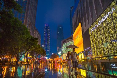 Pedestrians walk past fashion boutiques of Prada and Dolce&Gabbana in Jiefangbei CBD, also known as Jiefangbei Commercial Walking Street on a rainy night in Chongqing, China, 22 May 2015. clipart