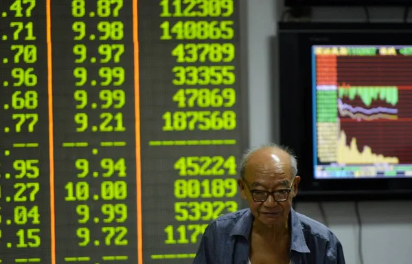 2015 日中国東部の浙江省杭州市の証券会社の家で株式 価格下落のためグリーン の価格を表示する画面の前に懸念している中国語の投資家が描かれています — ストック写真