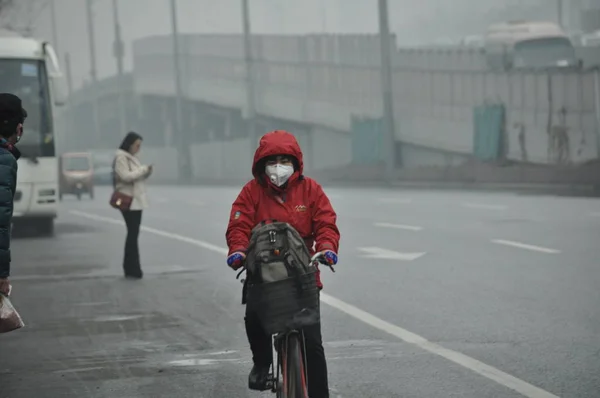 2015年12月14日 北京の重いスモッグの道路でフェイスマスクを着用したサイクリストが道路に乗る — ストック写真