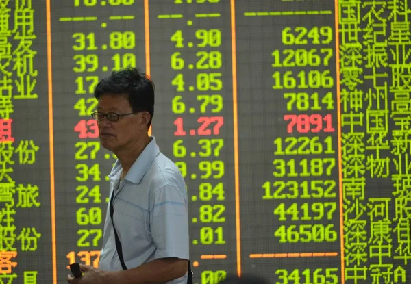2015年7月28日 在中国东部浙江省杭州市一家股票经纪公司 一位关心此事的中国投资者走过一个屏幕 显示股价 价格上涨为红色 价格下跌为绿色 — 图库照片