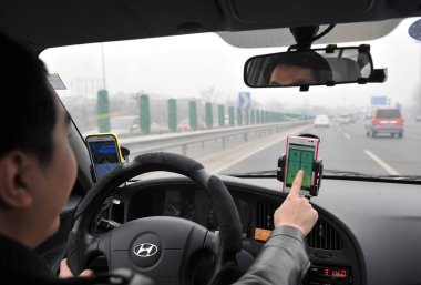 A Chinese taxi driver uses the taxi-hailing app Didi Dache on his smartphone while driving his car on a highway in Beijing, China, 3 March 2014 clipart