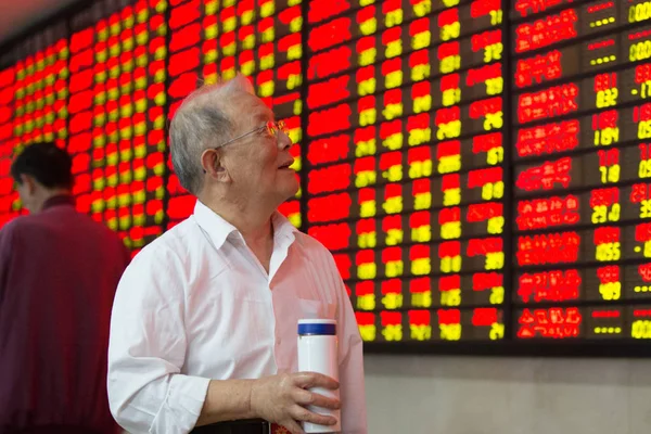 2015年10月20日 在中国东部江苏省南京市的一家股票经纪公司 一位中国投资者走过显示股价的屏幕 价格上涨为红色 价格下跌为绿色 时微笑着 — 图库照片