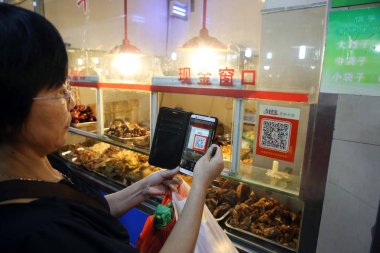 A Chinese customer scans a QR code via mobile payment service Alipay of Alibaba Group on her smartphone to pay for her purchase at a free market in Wenzhou city, east China's Zhejiang province, 14 September 2015 clipart