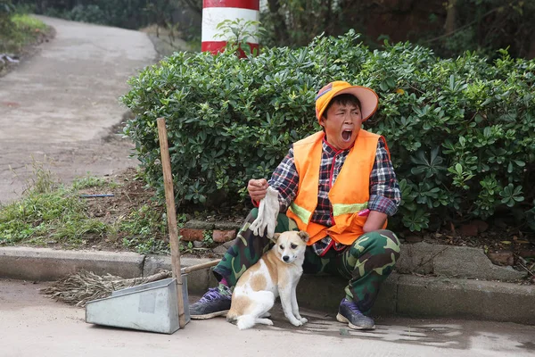 2015年11月15日 在中国东部的安徽省安庆市 中国一手工人方文英在清理街道时 在一只流浪狗旁边打哈欠 — 图库照片