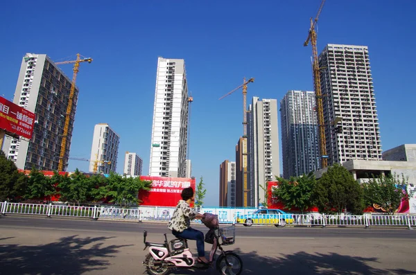 女性は 東シナの山東省 Rizhao 市で建設中の新しい住宅マンションの前に彼女の電気自転車に乗る 月2015 — ストック写真