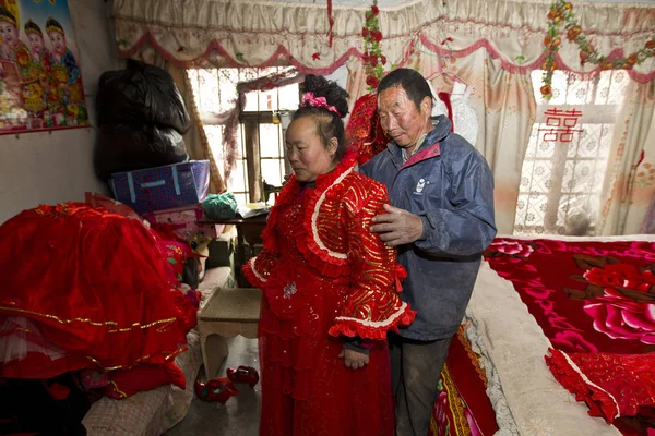 2014年4月11日 在中国东部山东省即墨市方格庄村 47岁的中国村民项俊峰在丈夫朱正良的协助下 在家里穿上了一件红色婚纱 — 图库照片