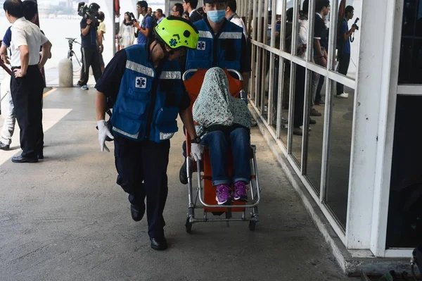 高速フェリーが壊水に墜落して負傷した車椅子に座っていた乗客は 2014年6月13日に中国のマカオのフェリーターミナルに到着した後 救助隊によって護衛されます — ストック写真