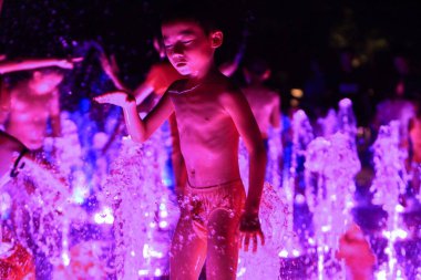 Young Chinese kids enjoy splashes of water to cool off in a music fountain on a sweltering day at night in Foshan city, south Chinas Guangdong province, 20 July 2014. clipart