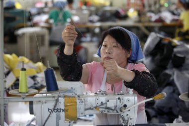 female Chinese worker sews clothes to be exported to South Korea at a garment factory in Huaibei city, east Chinas Anhui province, 16 July 2014 clipart