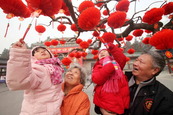 祖父母によって保持されている二人の少女は 2012 日今後の春祭りや北京 中国の旧正月を祝うために寺フェアの準備でツリーに表示されている赤い提灯に興味を示す — ストック写真