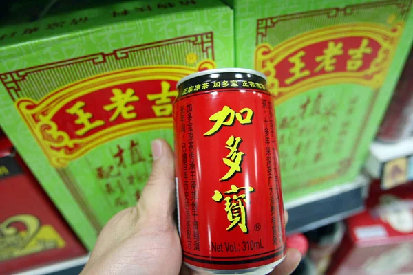 中国の顧客は 2013年12月20日 中国上海のスーパーマーケットで広州製薬ホールディングスのウォン カトハーブティーのカートンの前で JiaduobaoグループのJiaduobaoハーブティーの缶を示しています — ストック写真