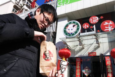 A pedestrian holds KFC fast food outside a Little Sheep restaurant in Tianjing, China, 2 February 2012 clipart