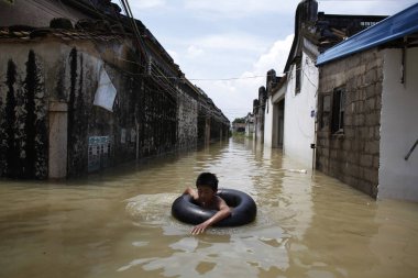 A Chinese young boy uses a scrap tire inner tube as a simple life preserver flooding on a street after the city battered by typhoon Utor in Shantou, northeast Chinas Guangdong province, 19 August 2013 clipart
