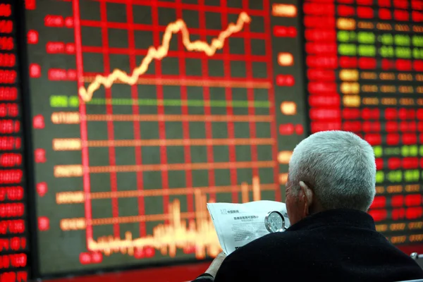 投資家は 株式の価格を示す画面の前で新聞を読みます 価格上昇のための赤と価格下落のためのグリーン Huaibei 市の株式仲買家での株価指数 東中国安徽州 月2012 — ストック写真