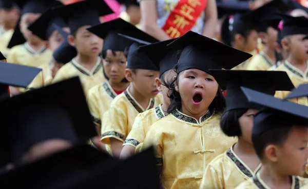 伝統的な衣装を身にまとった中国の若い学生が あくびの中で ジンジャン市の Gaoxia 小学校で孔子の生誕2563Rd 周年を記念して 他の人々の間で 学術的な帽子をかぶっていた — ストック写真