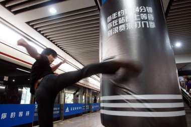 A passenger kicks an advertisement for Adidas in the shape of a punching bag at the Xujiahui Subway Station of the Shanghai Metro Line 1 in Shanghai, China, 8 August 2011 clipart