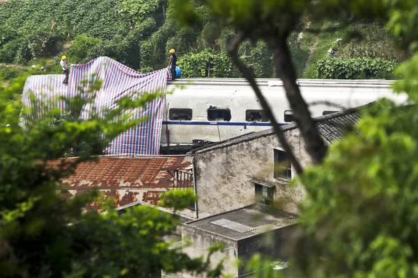 Workers cover a damaged train carriage to be removed with a sheet on the site of the deadly train collision in Wenzhou city, east Chinas Zhejiang province, 26 July 2011