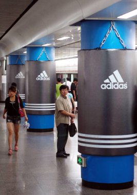 Passengers walk past advertisements for Adidas in the shape of punching bags at the Xujiahui Subway Station of the Shanghai Metro Line 1 in Shanghai, China, 8 August 2011 clipart