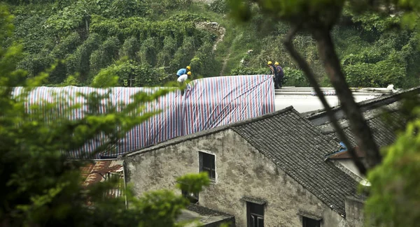 Workers cover a damaged train carriage to be removed with a sheet on the site of the deadly train collision in Wenzhou city, east Chinas Zhejiang province, 26 July 2011