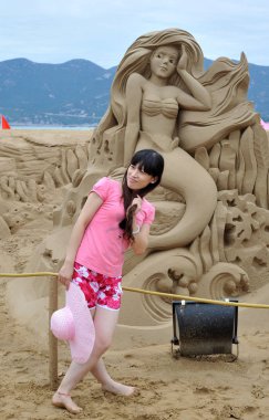 A visitor poses in front of a sand sculpture of Mermaid at Disney theme sand sculpture exhibition in Zhoushan, east Chinas Zhejiang Province, 24 September 2011 clipart