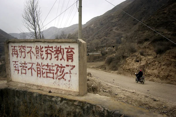 一位中国村民骑着摩托车走过一个口号 意思是即使贫困恶化 教育也远离贫困 在定西市民县小寨村门口 让孩子们远离悲惨生活 — 图库照片